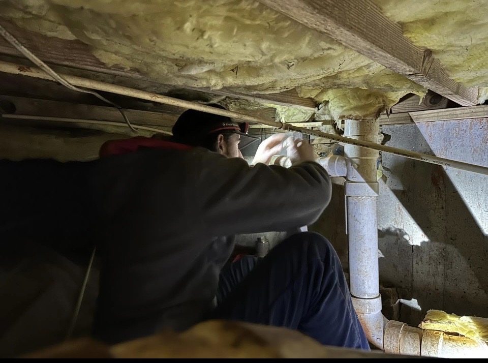 Plumber repairing pipes in a crawl space